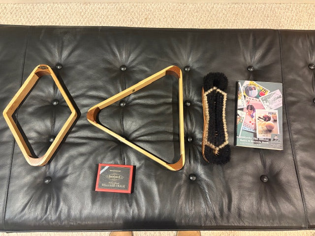 Pool table accessories including triangle rack, cue tip, and magazine on a black leather bench.