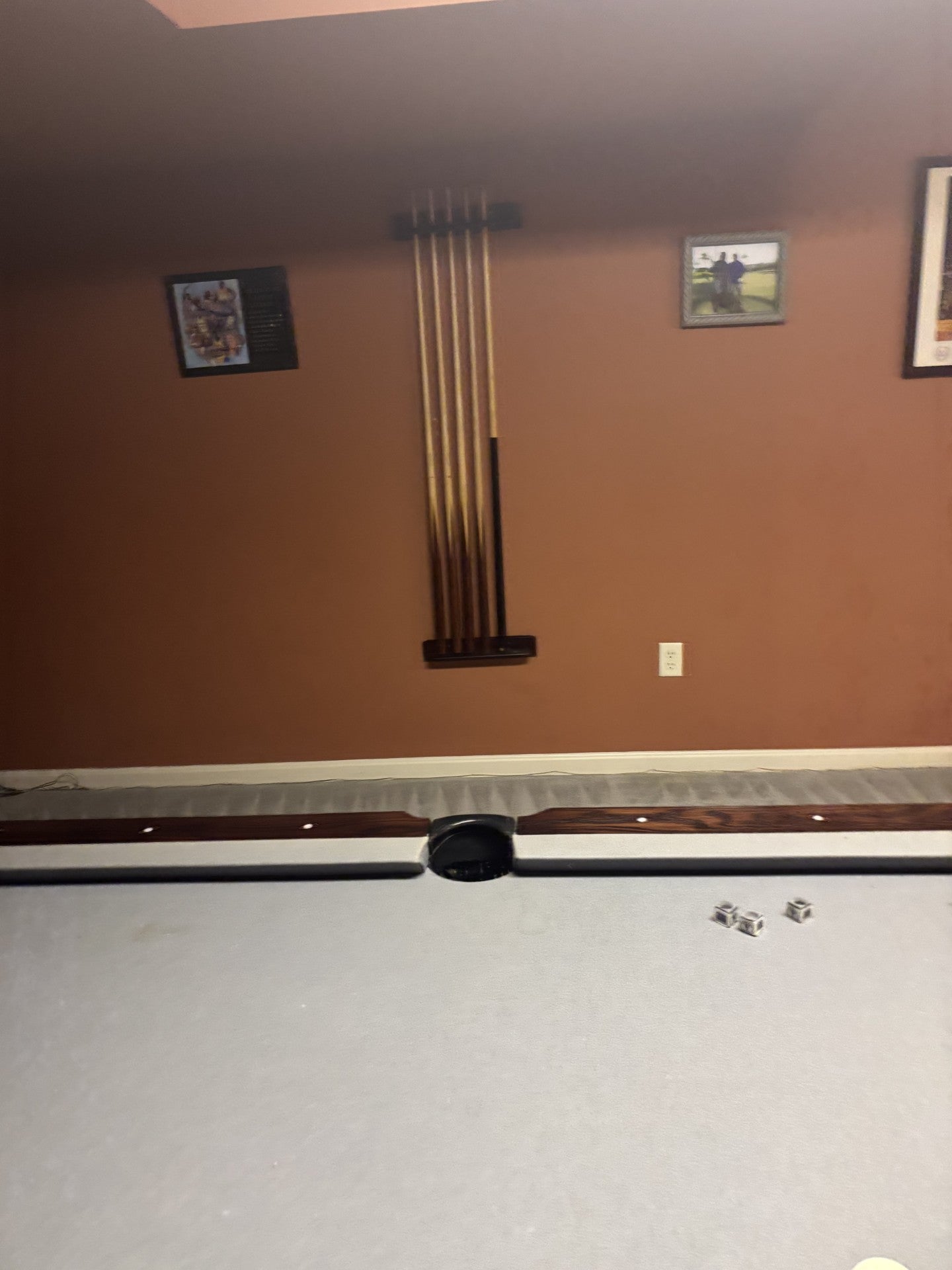 Pool table with pool cues leaning against a wall in a room.