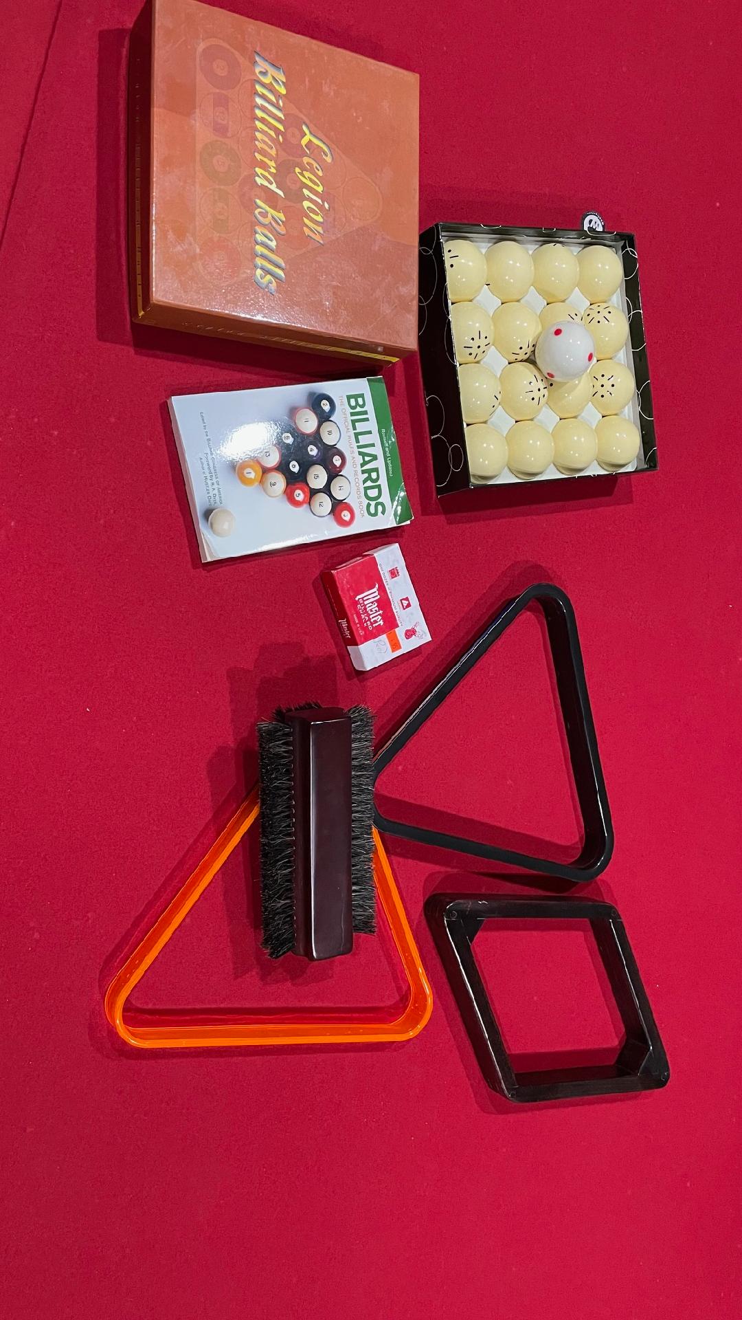 Pool table accessories including balls, triangle rack, and brush on a red background
