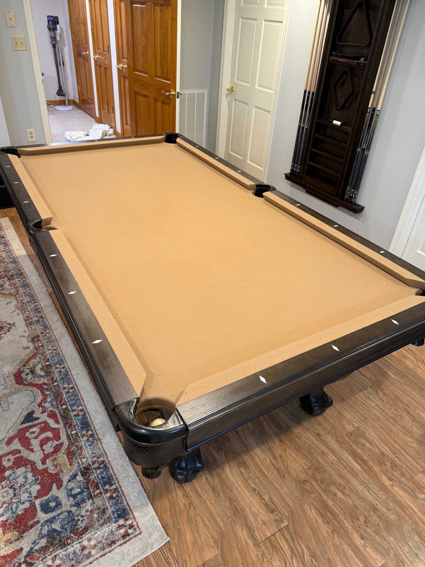 Pool table with beige felt surface in a room with wooden flooring and a rug.
