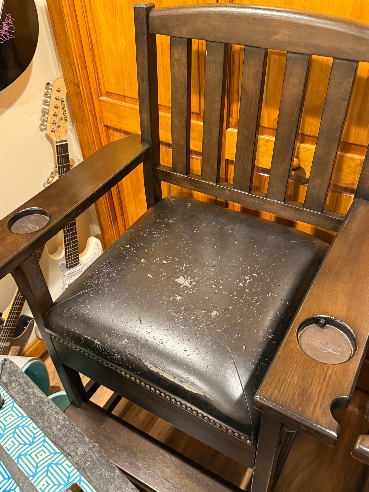 Close-up of a chair with a wooden backrest and metal armrests, showing signs of wear.