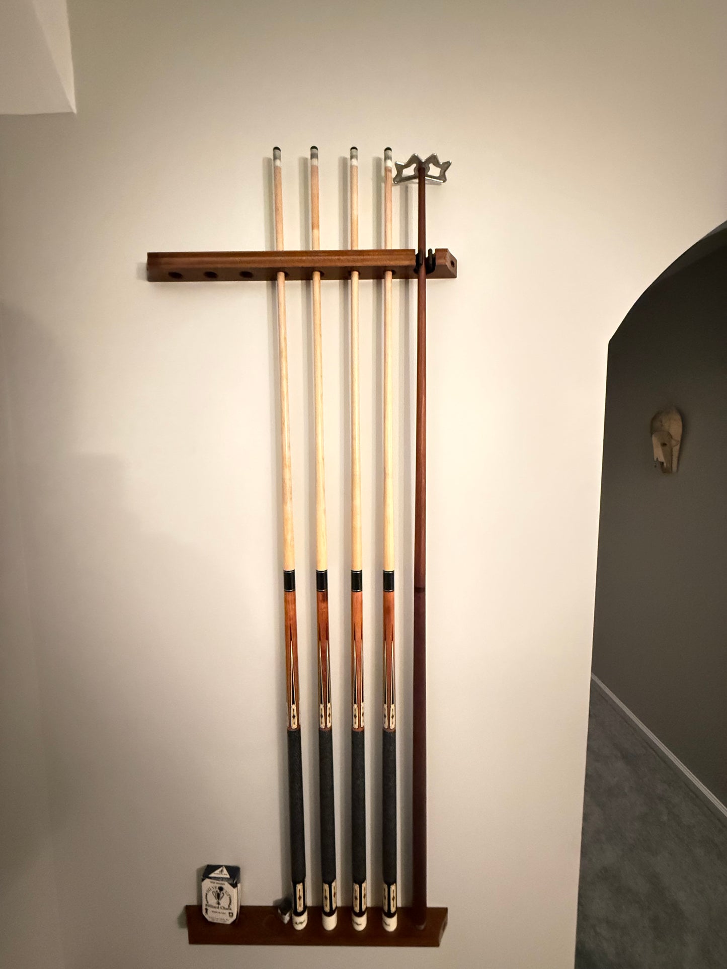 Wall-mounted pool cue holder with multiple cues on a plain wall.