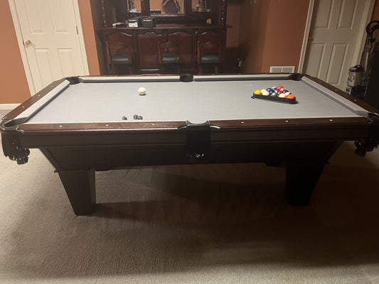 Pool table with balls and cues in a room with a dining area in the background