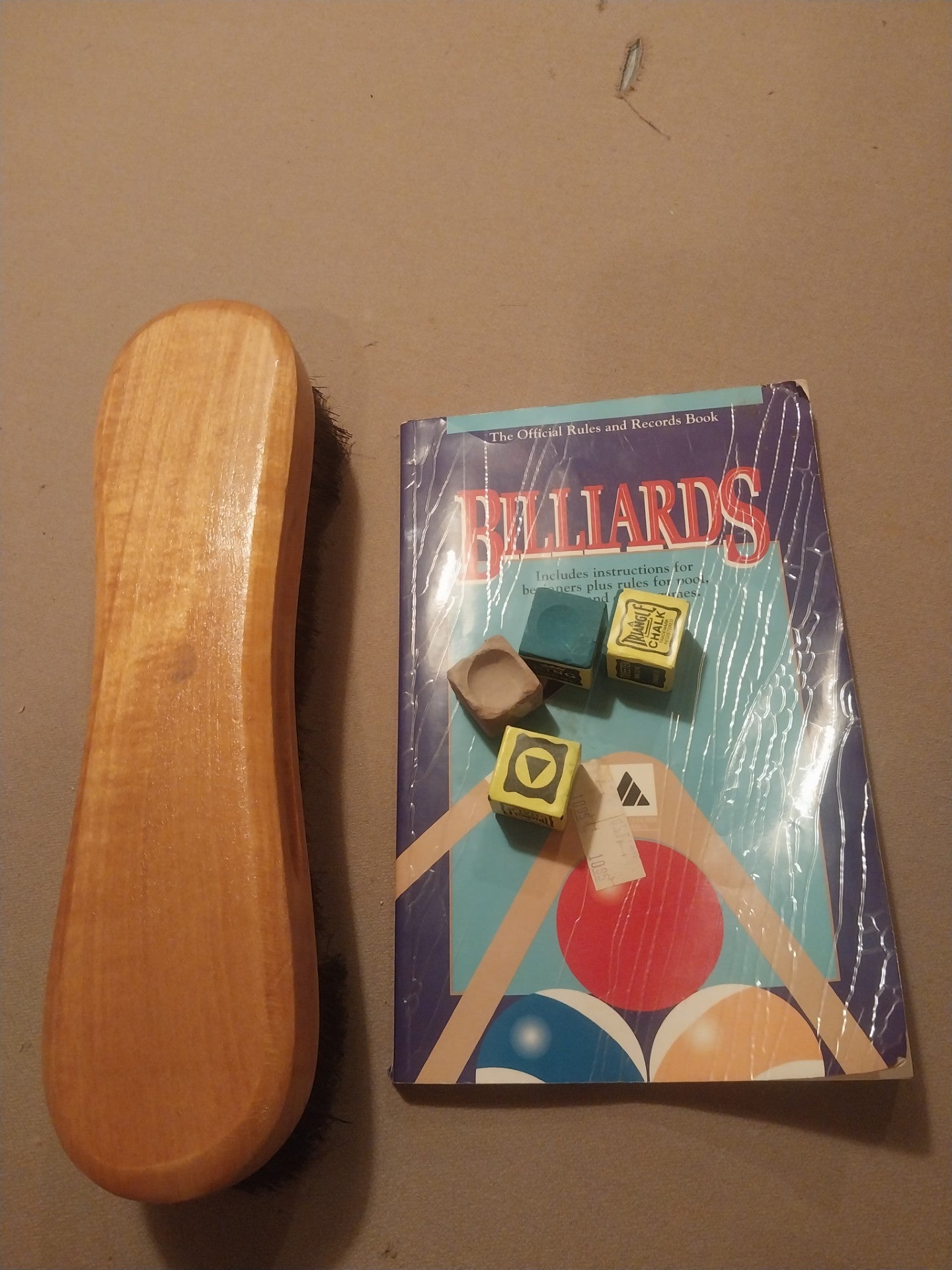 Wooden pool cue case next to a 'Billiards' book on a brown surface