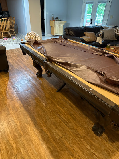 Pool table with brown felt cover in a room with wooden flooring and furniture.